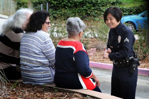 Female Asian LAPD officer talks to three women who are sitting down